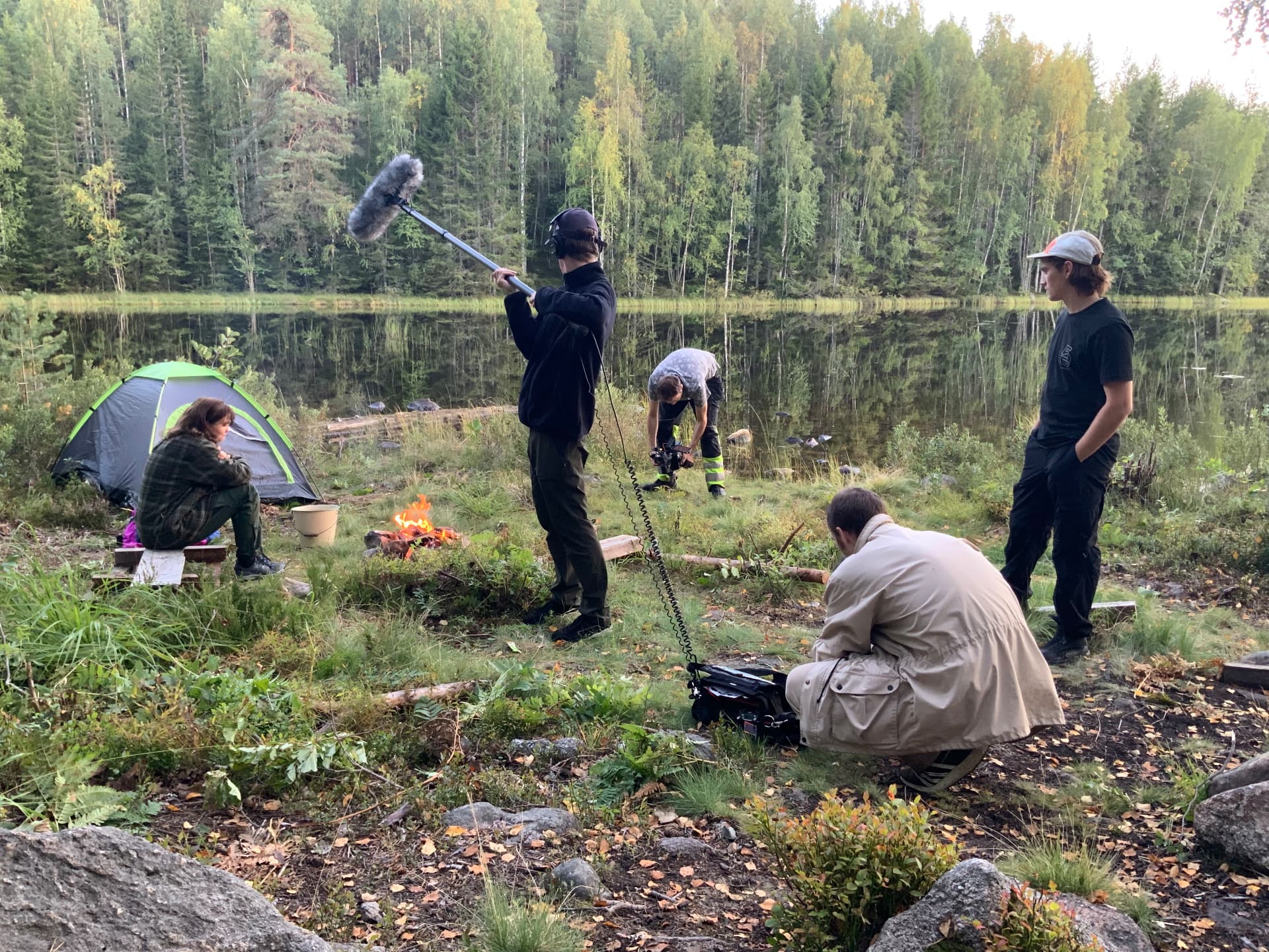 Crewet filmar en scene vid en lägereld vid en sjö i skogen